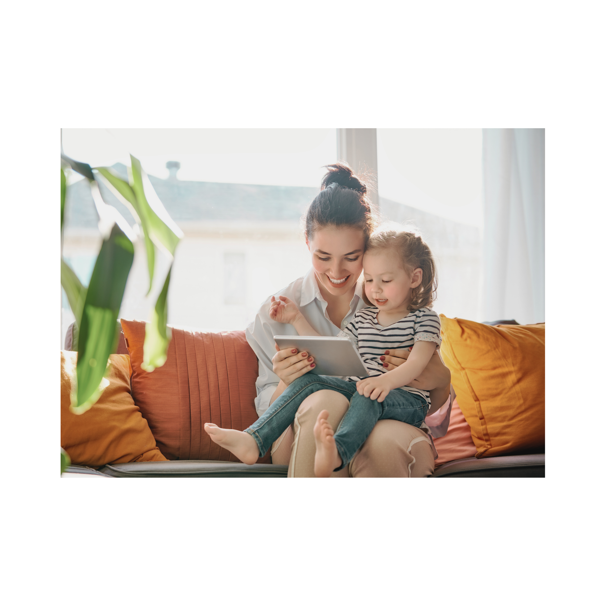 A mom and her young daughter sitting together on a sunlit couch