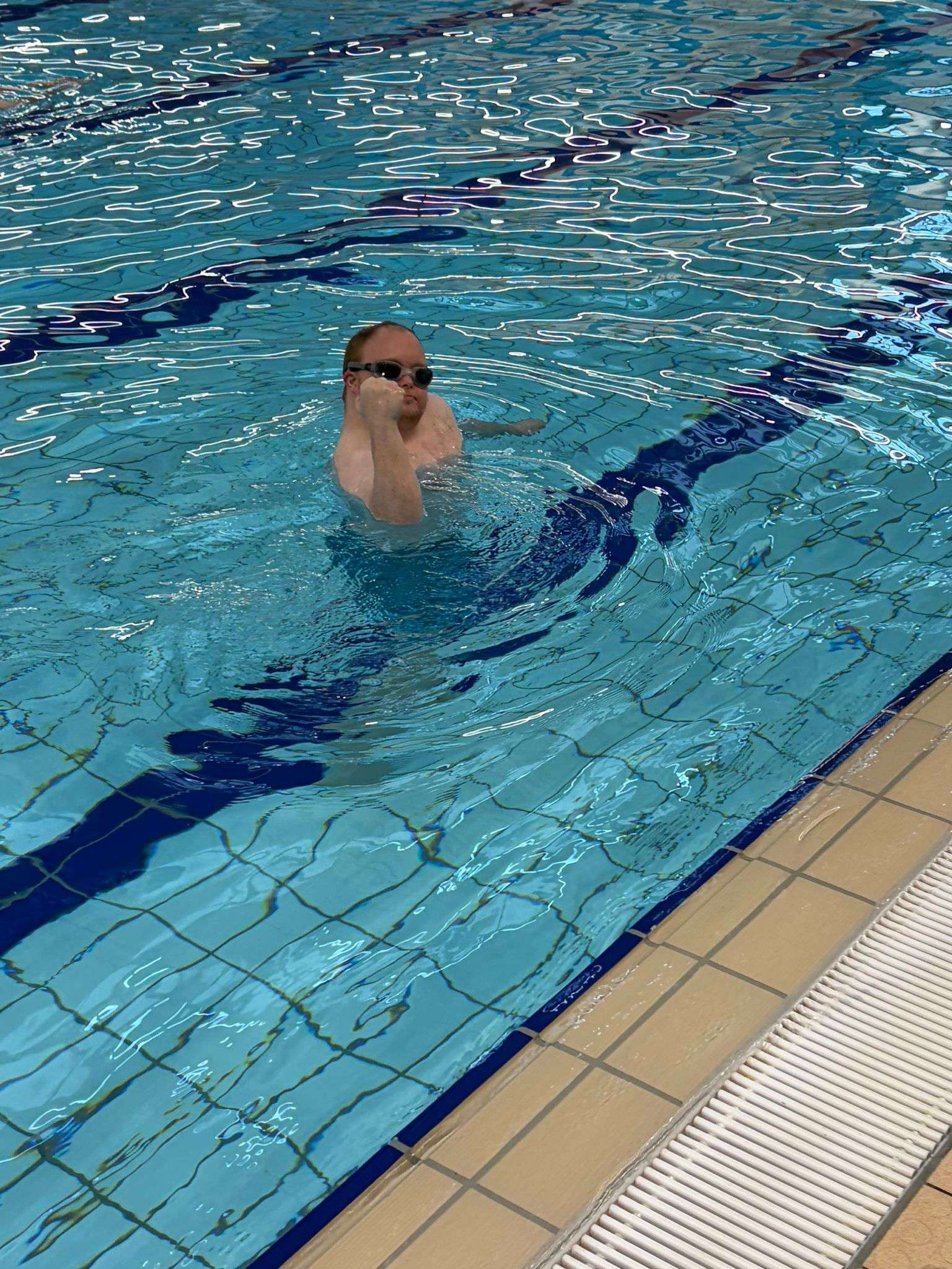 Someone we support swimming confidently in an indoor pool wearing goggles.