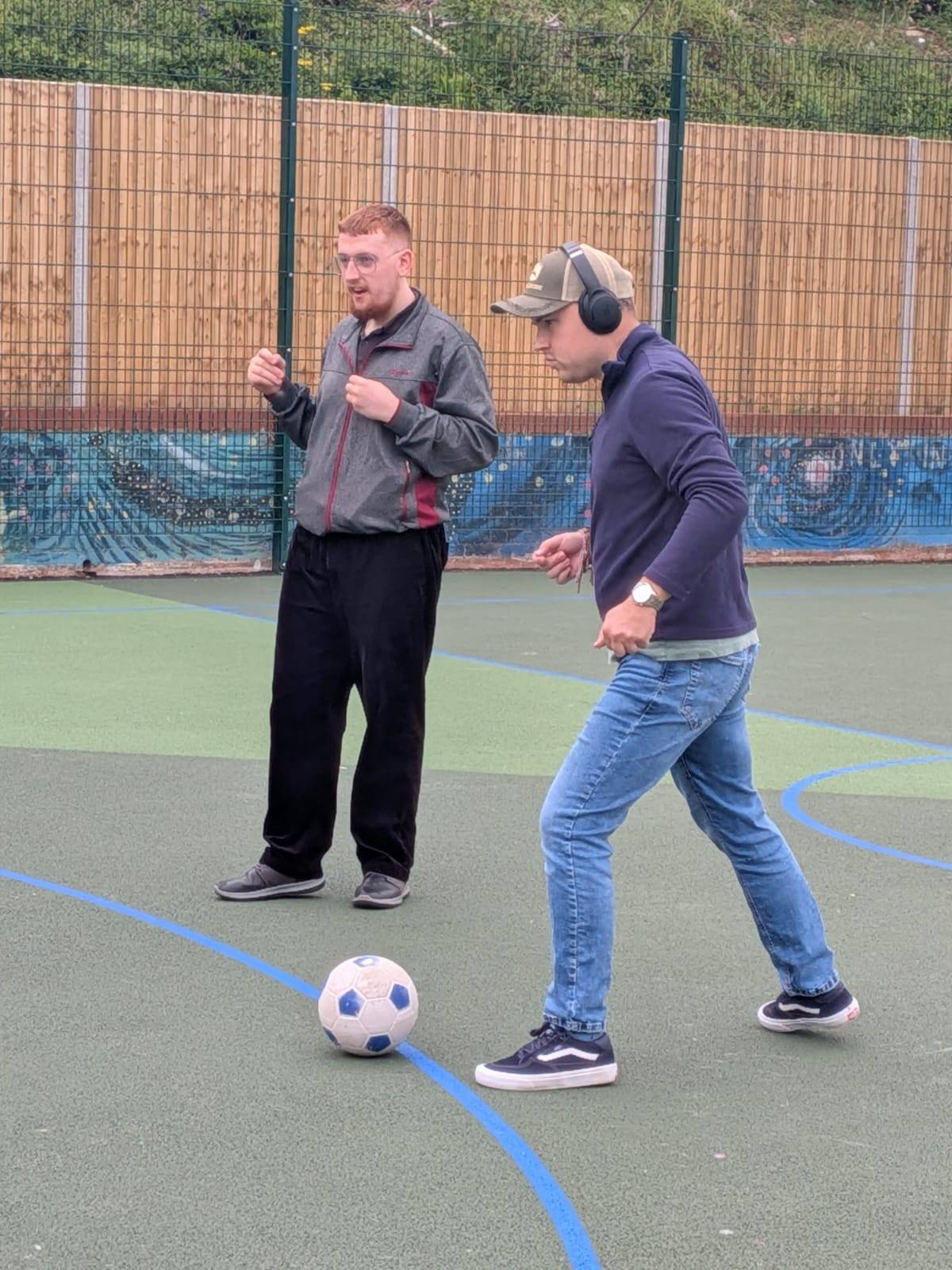 Someone we support and a support worker enjoying a game of football together on an outdoor court.