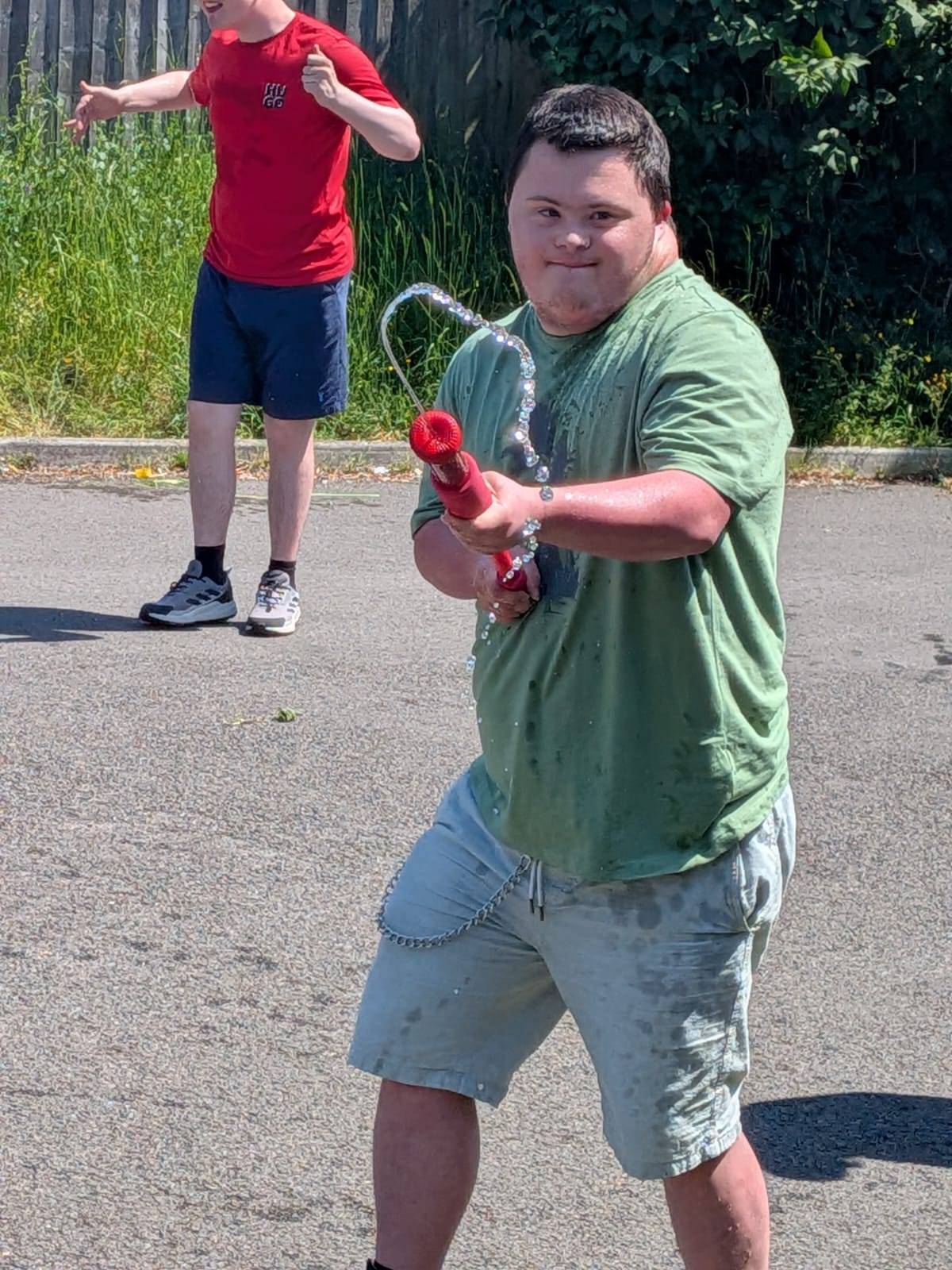 A young man we support smiling during a fun summer water fight outdoors.