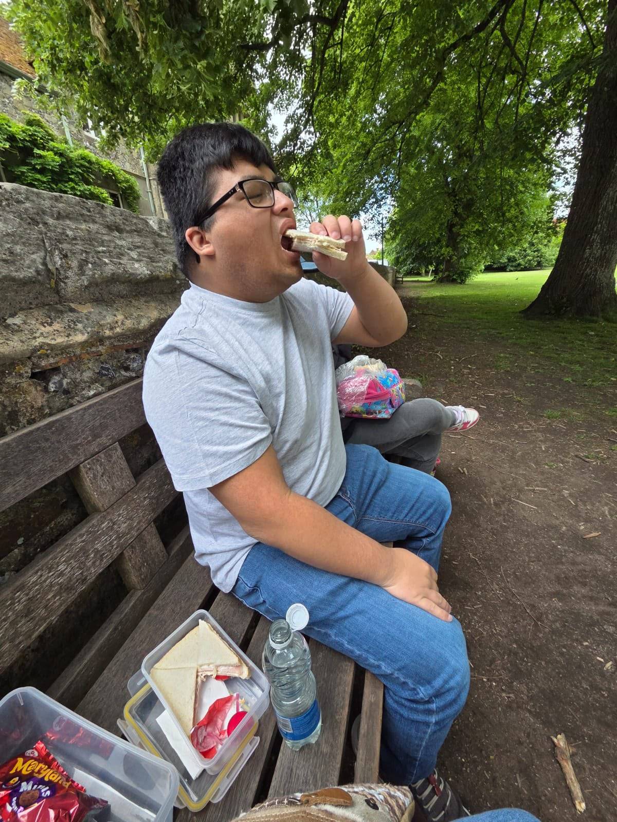 Someone we support enjoying a packed lunch on a bench during a day out in the park.