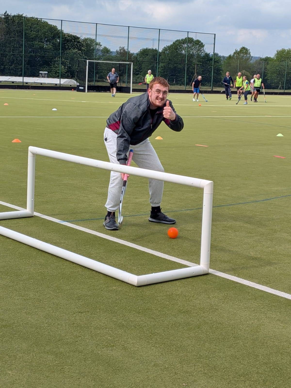 A young man we support giving a thumbs up during a hockey session on an astroturf pitch.