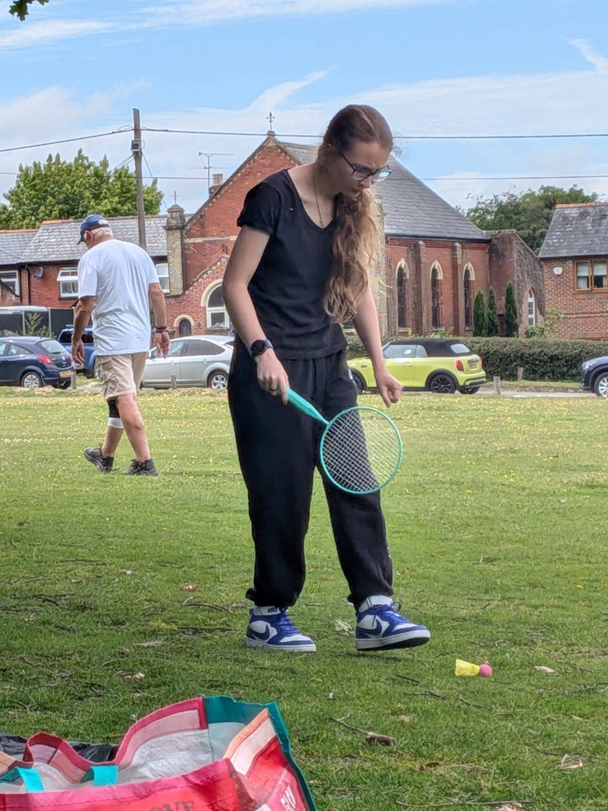 Someone we support playing badminton with a racquet and shuttlecock on a grassy field.
