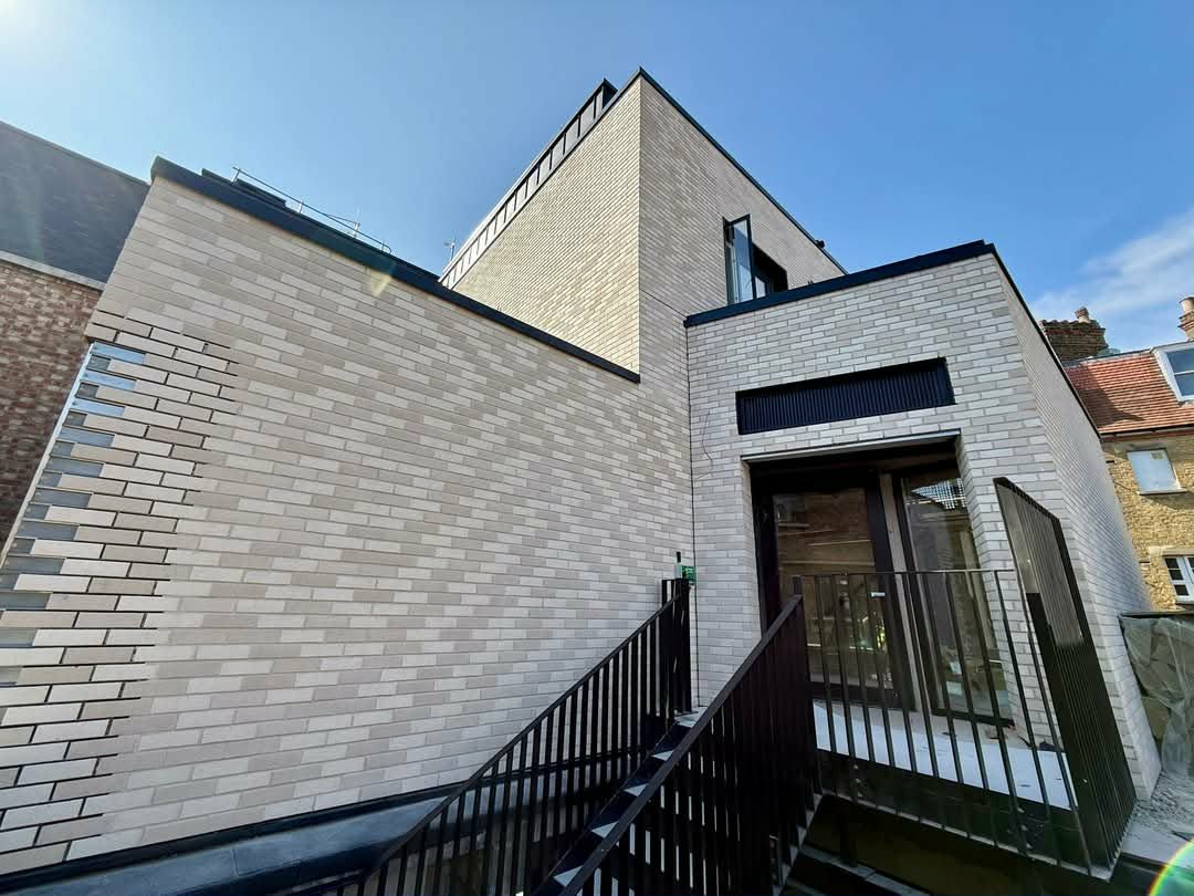 Completed brick cladding system on a contemporary new-build — light cream brick-slip façade with sharp parapet detailing and metalwork