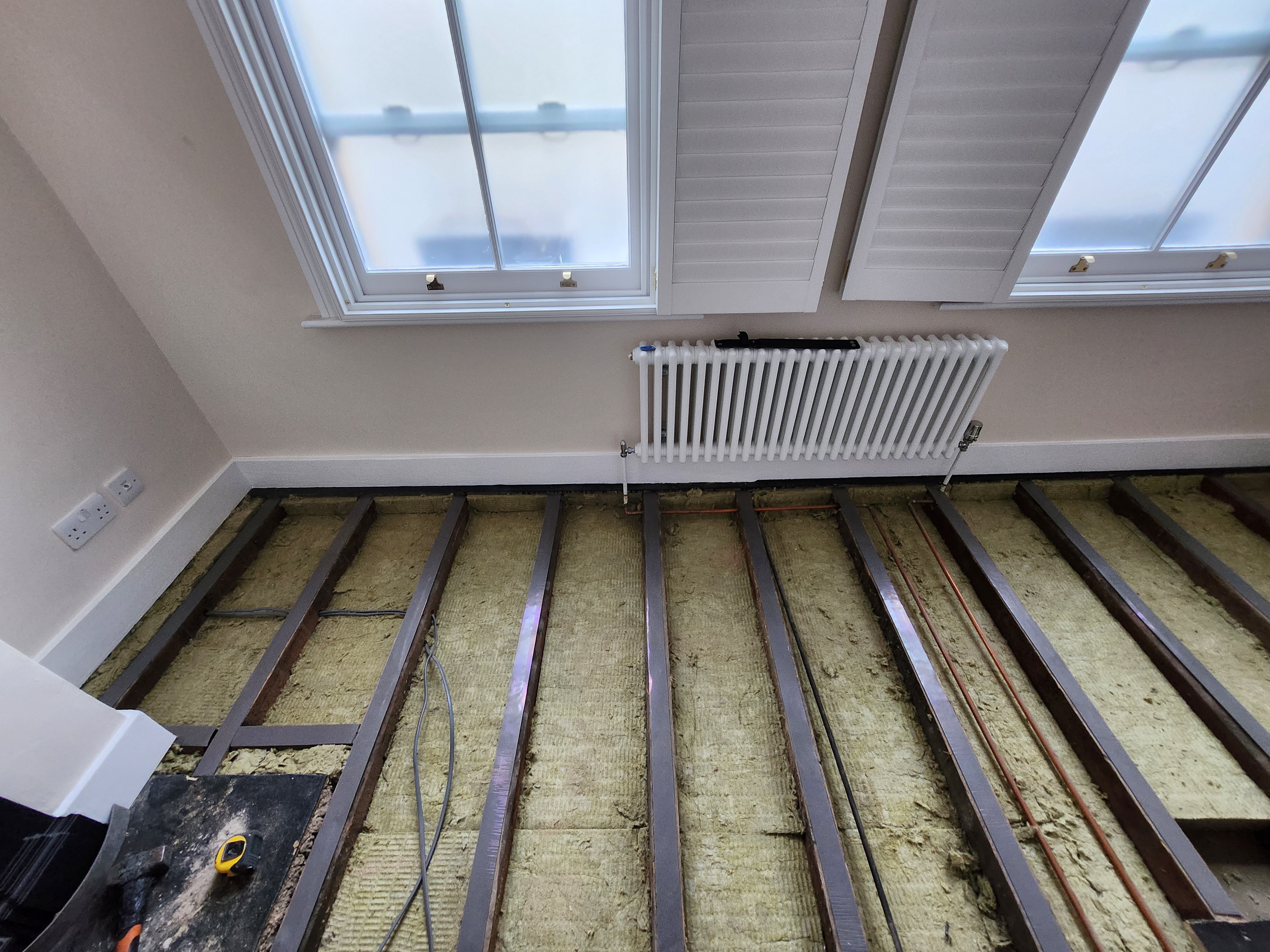Stage 3 — rockwool fully installed between joists with resilient acoustic bars fixed across the joists to decouple the new floor structure