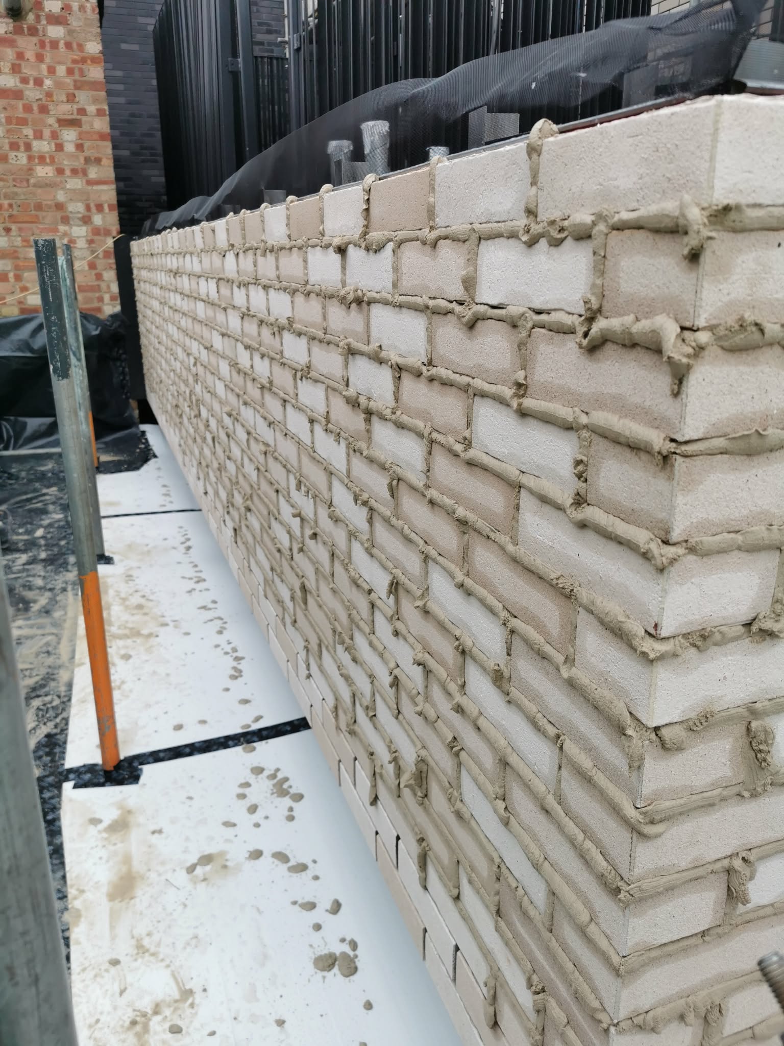Brick-slip panels being installed onto the metal rail system over the mineral wool insulation and breather membrane — ventilated façade build-up