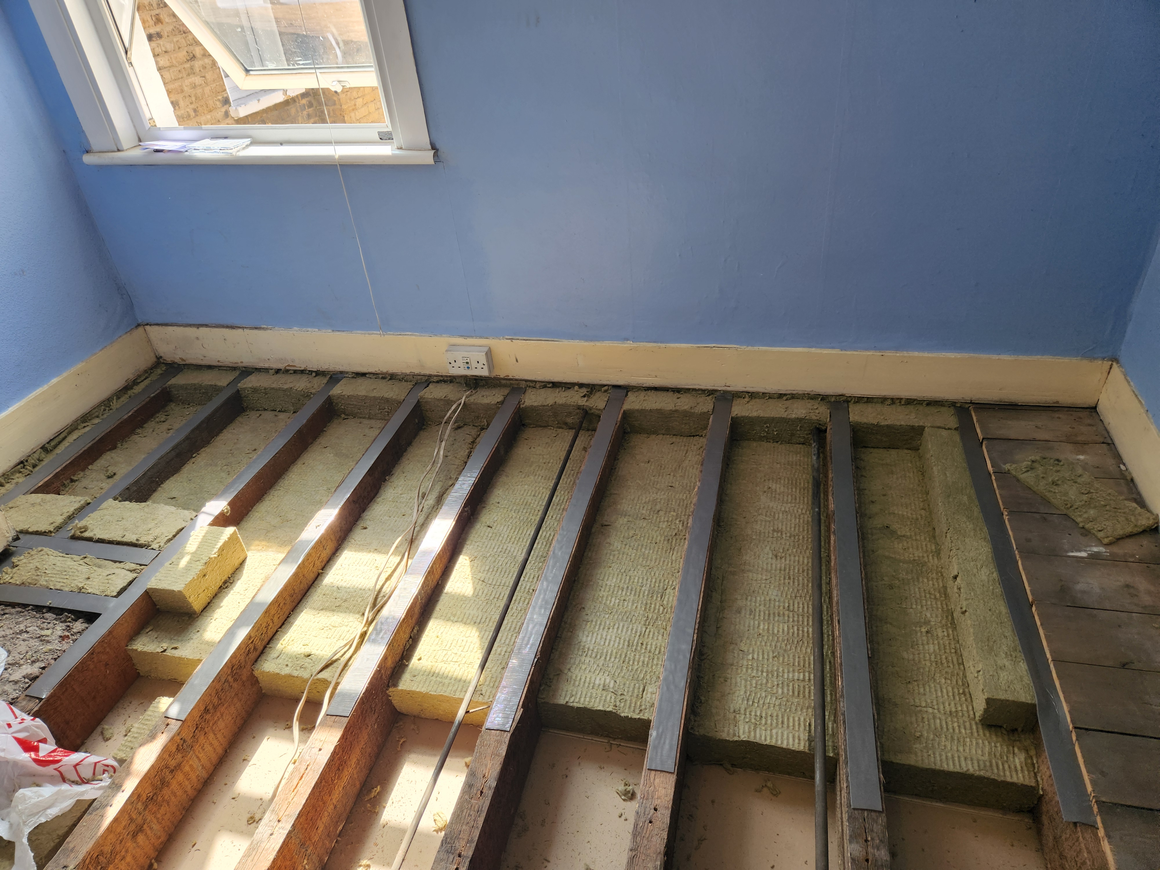 N17 project · blue bedroom — same four-stage build-up: floor stripped, mineral wool between joists, resilient acoustic bars decoupling the new deck from the structure