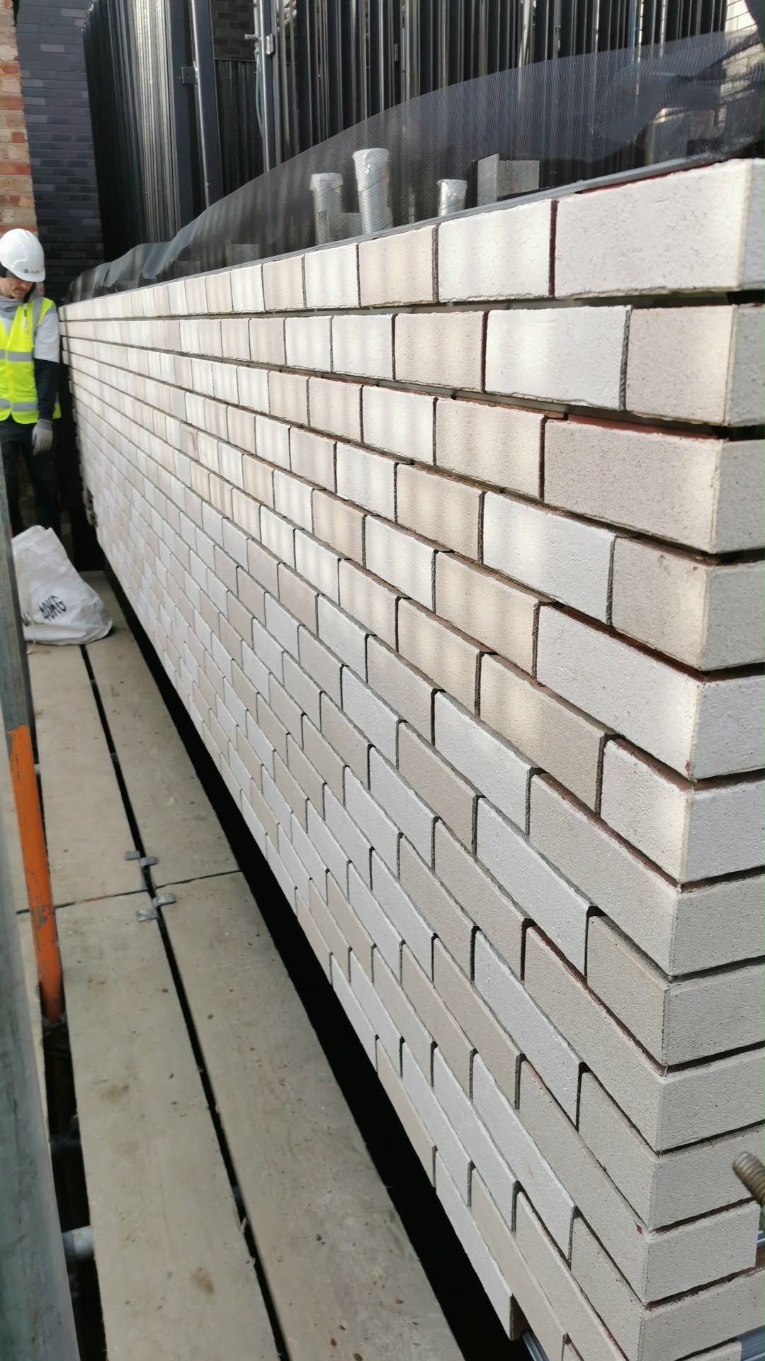 Close-up of the brick-slip cladding system — brick slips bonded onto insulation panel substrate with mortar joints raked back ready for finishing