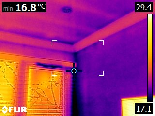 Wall / ceiling corner with vertical service pipe — concentrated cold spot at the corner junction indicating a localised thermal bridge plus a cooler signal along the pipe run