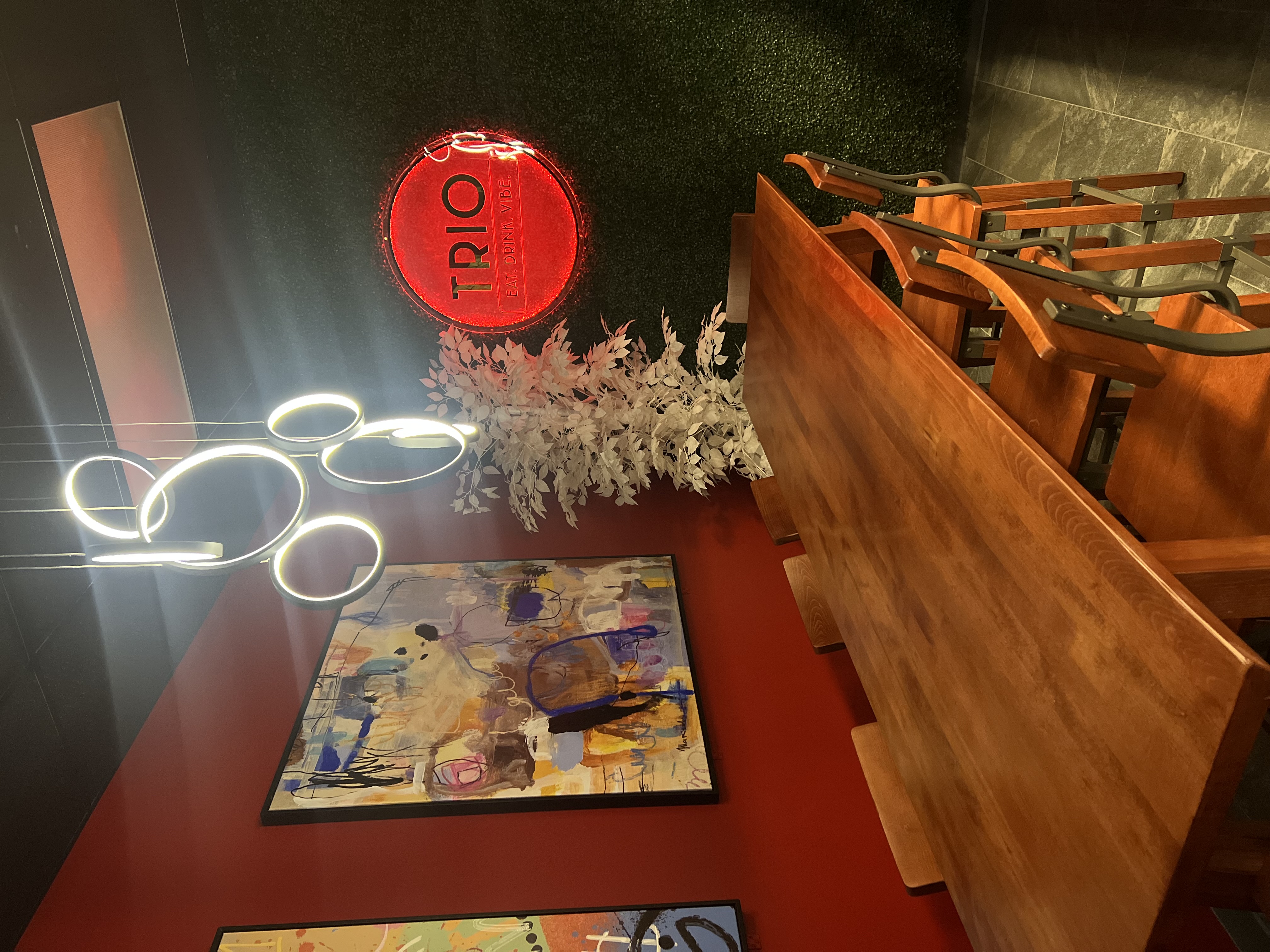 Inside Trio — red walls, neon, ring chandelier and a long wood table