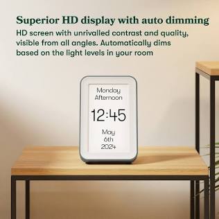 A high-contrast HD day-and-date clock on a side table, displaying 'Monday Afternoon, 12:45, May 6th 2024'