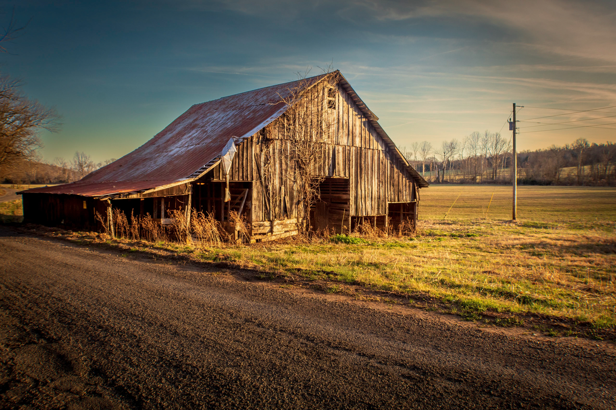 Color photograph of a weathered barn with a light pole against a sunset sky