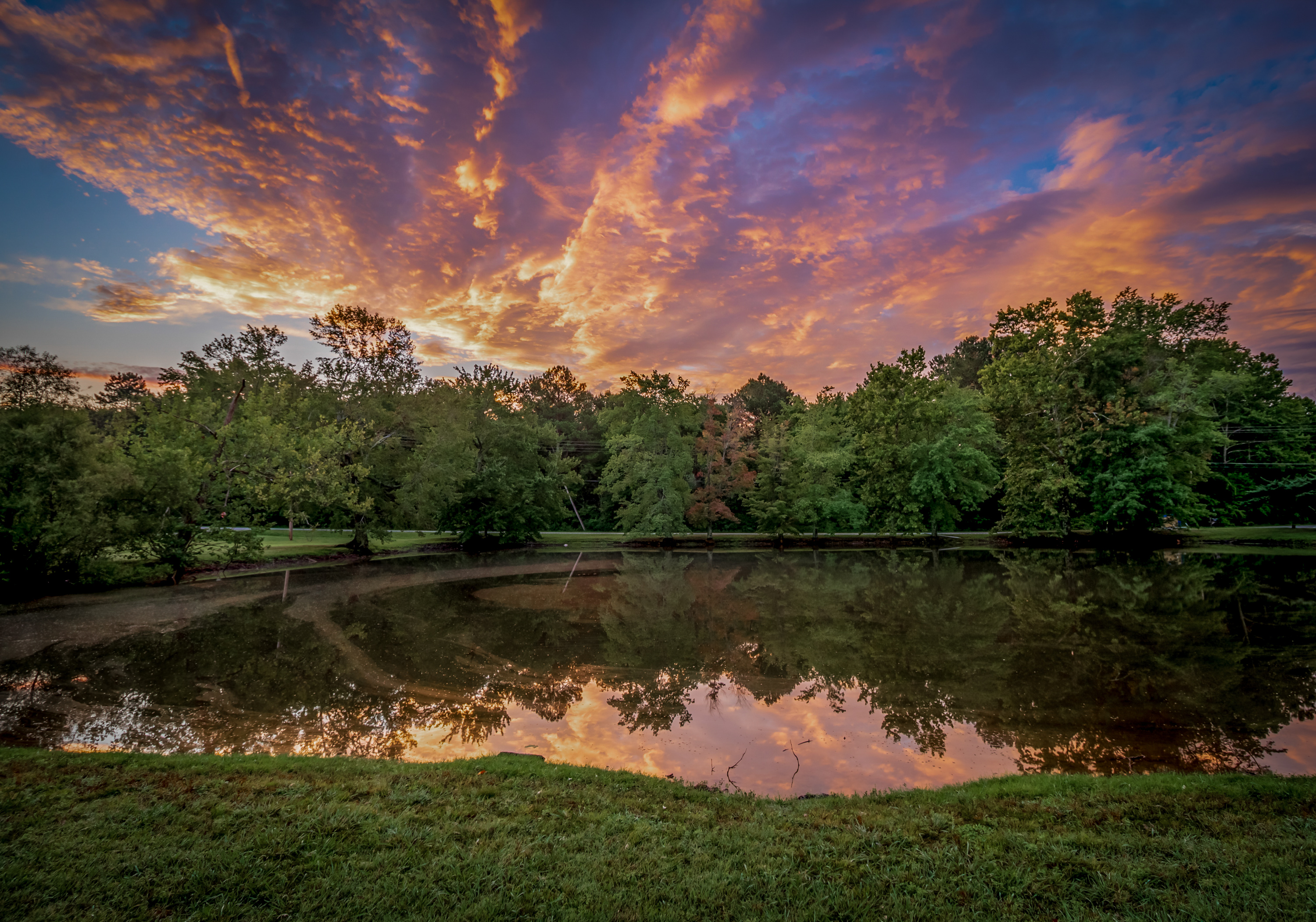 Color photograph of a sunset lake reflection framed by trees and dramatic clouds