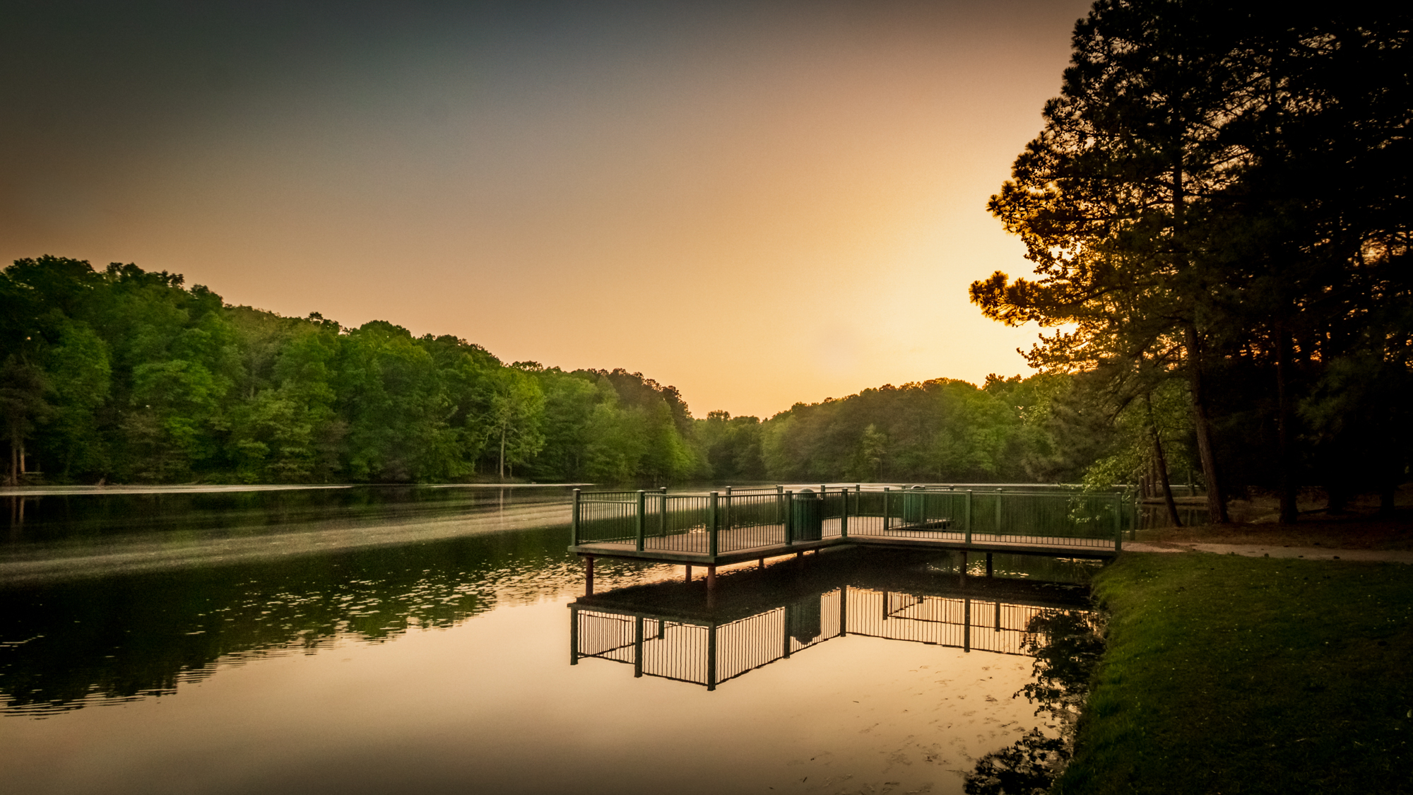 Color photograph of a dock extending across a lake at golden hour