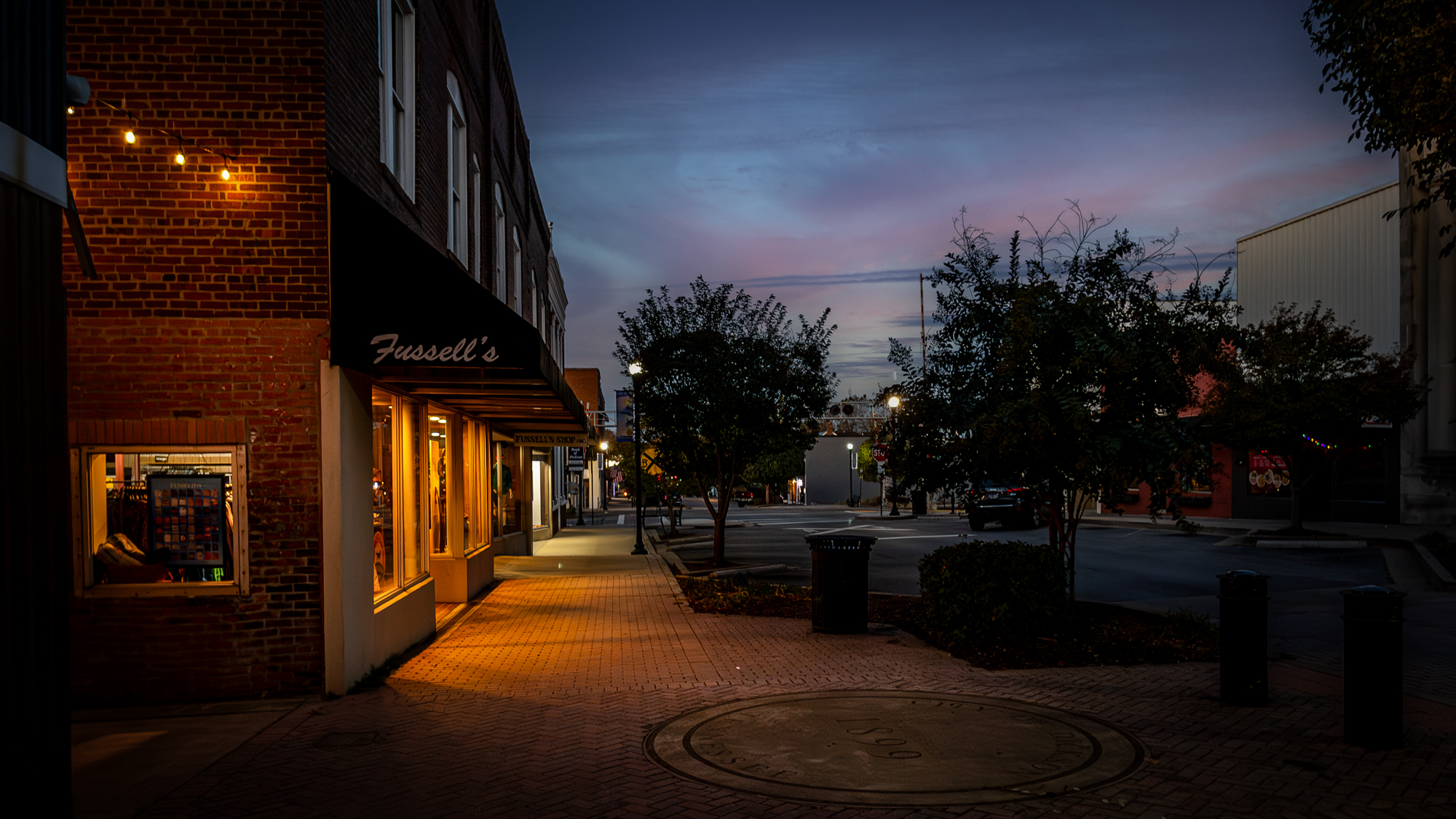 Color photograph of Fussell's storefront and a quiet downtown sidewalk at dusk
