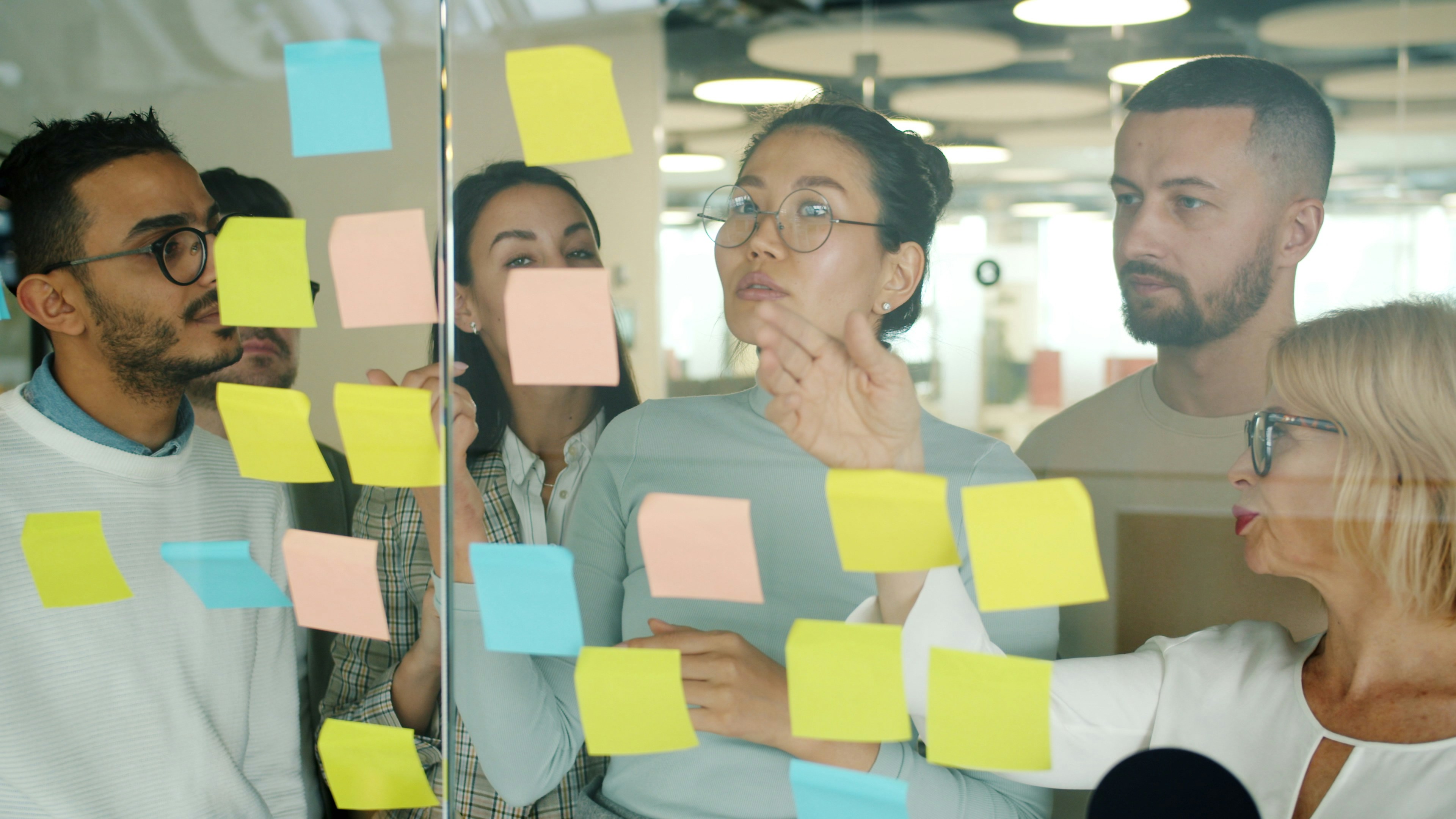 Office team gathered around a glass wall covered in sticky notes — a familiar visual of small businesses trying to manually track and organize information.